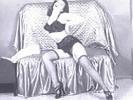A girl with long black hair wearing a bathrobe is laying down on a couch. She gets up and opens the robe, showing she is only wearing undies, nylons and high heels.