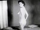 In the first scene of this vintage black and white movie we see a young woman posing naked in front of the camera. She stands up at first and then kneels down on the floor. In the next scene a naked girl sits in front of a fire reading a book.